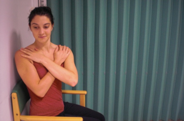 Person seated with hands crossed across chest. Torso turned to face one side.