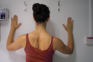 Person standing with hands against a wall in front. A visible crease between shoulder blades in back.
